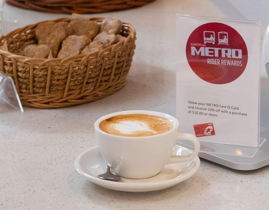 Cup of coffee on retail counter next to METRO Rider Rewards promotional card.